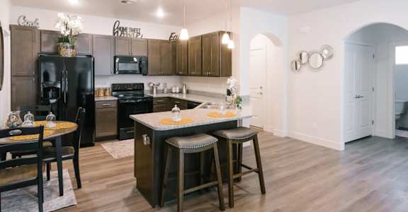 A kitchen with a black fridge and wooden floors.