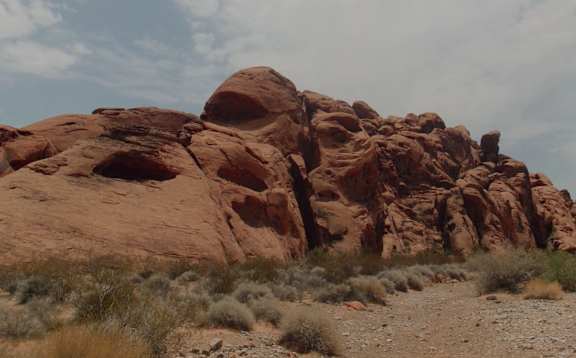 A large red rock formation with a few small bushes in front of it.