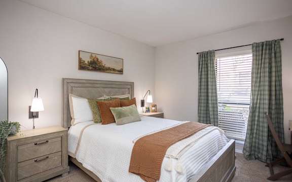 A bedroom with a large bed, a nightstand with a lamp, and a painting on the wall.