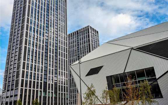 A modern building with a curved metallic facade stands in front of two taller buildings.