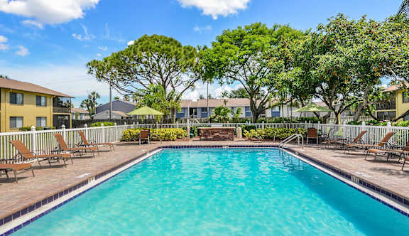 A swimming pool surrounded by trees and chairs.
