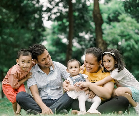a family of five sitting on the grass in a park