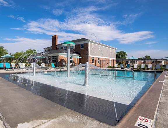 A large outdoor swimming pool with a waterfall feature and a building in the background at Gramercy Apartments, Indiana