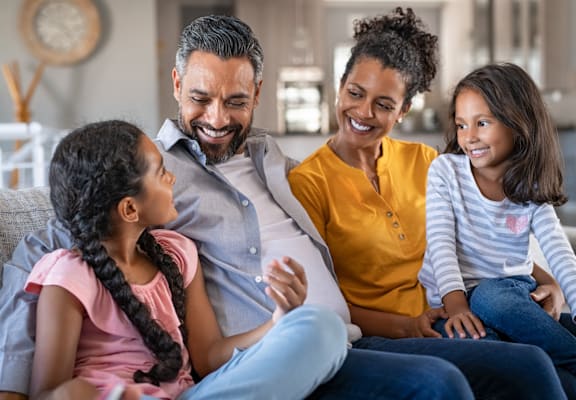 A family of four is sitting together on a couch.