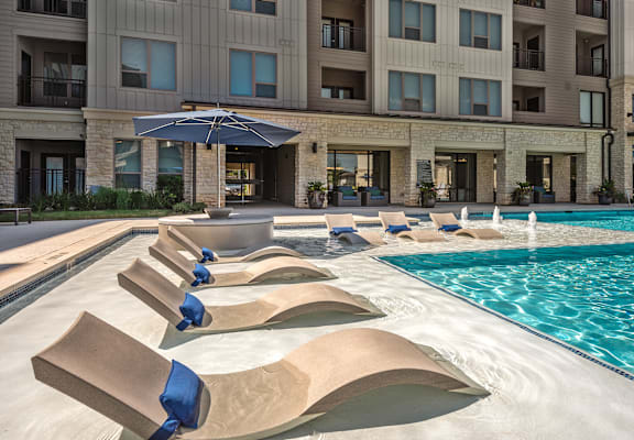 A large swimming pool with sun loungers in front of a hotel.