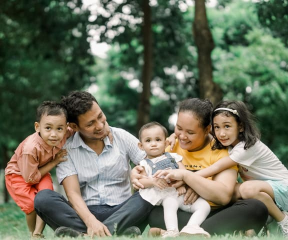 a family of five sitting on the grass in a park