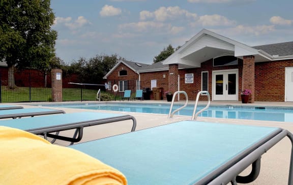 apartment swimming pool with two light blue lounge chairs a clubhouse in the background