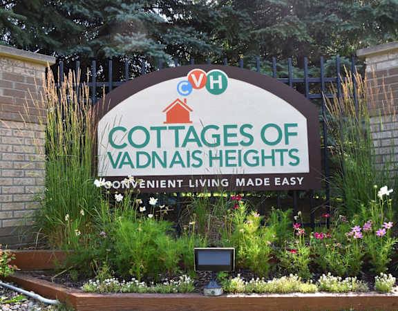 A sign for Cottages of Vadnais Heights is displayed in front of a garden.
