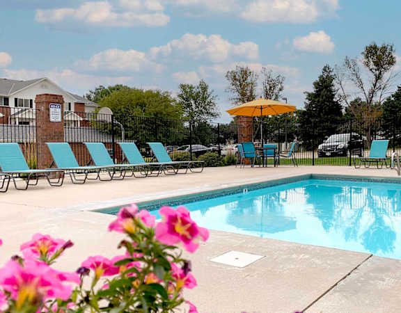A pool surrounded by chairs and flowers with a building in the background.
