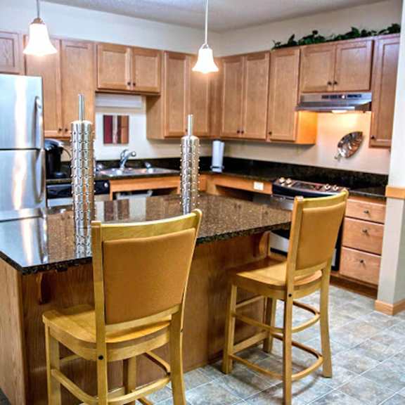 A kitchen with a refrigerator, two chairs, and a countertop.