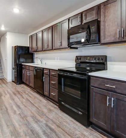 kitchen with dark wood cabinets black appliances wood flooring and an island
