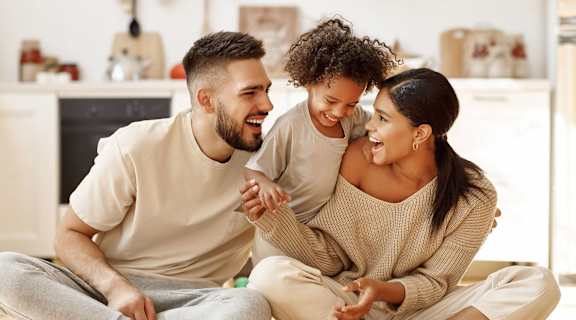 A man and a woman are sitting on the floor with a child, all are smiling and appear to be happy.