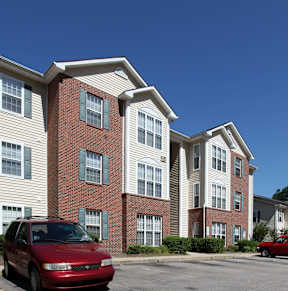 A red car is parked in front of a two-story apartment building.