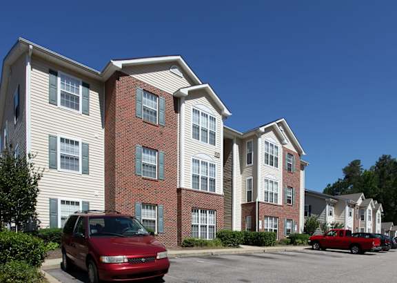 A red car is parked in front of a two-story apartment building.