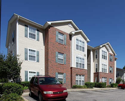 A red car is parked in front of a two-story apartment building.