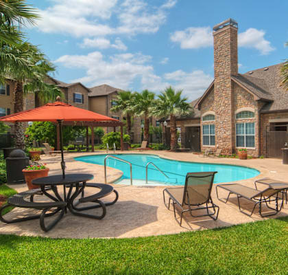 A pool surrounded by chairs and a table with a house in the background.