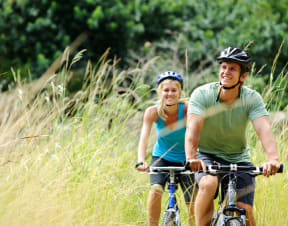 a man and a woman riding bikes through a grassy field