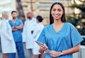 a woman in blue scrubs holding a tablet and smiling at the camera