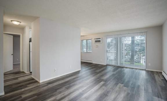 the living room and dining room of an apartment with wood floors and a large window