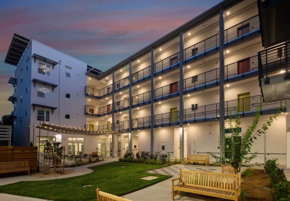 Interior courtyard at Lavender with large green space, patio, and walkways illuminated with string lights and hallways lighting. 
