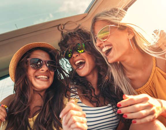 Three women wearing sunglasses and hats are laughing and enjoying themselves in a car.