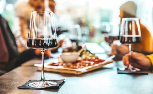 a glass of red wine on a table with people eating pizza