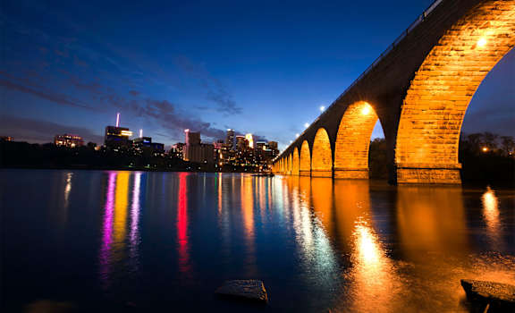a view of the stone arch bridge at night with the lights of the city in the background