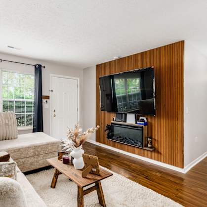A living room with a couch, a coffee table, and a television on a wooden wall.