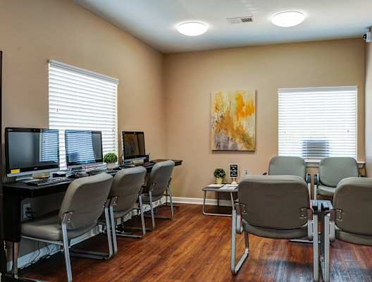 A room with a desk and chairs with a painting on the wall.