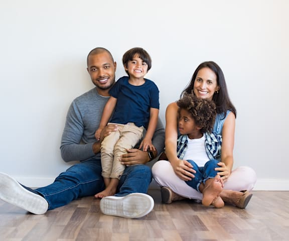 a family of four sits on the floor against a white wall