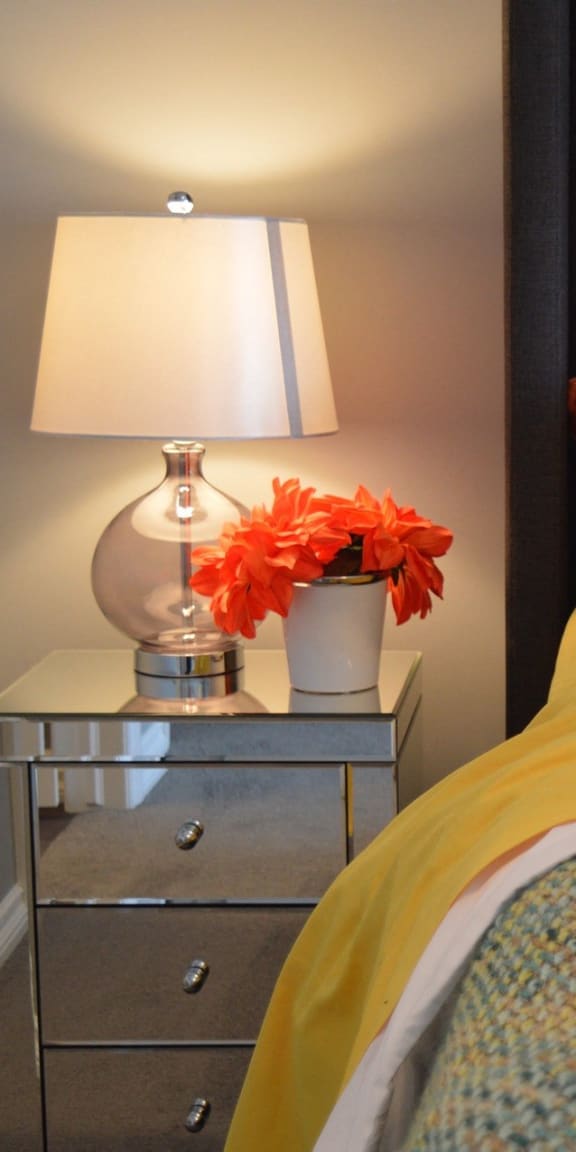 a bed with yellow sheets and pillows and a table with a lamp and flowers