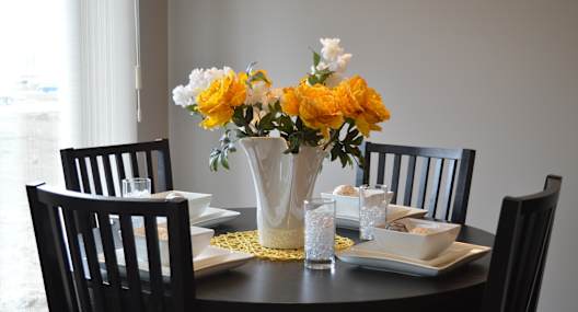 A dining table set with a vase of flowers in the middle.