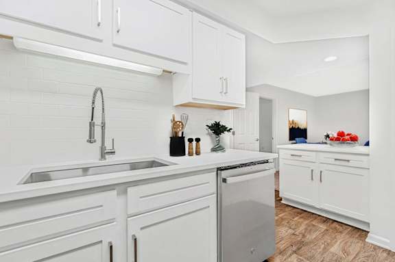 A white kitchen with a stainless steel dishwasher and a sink.