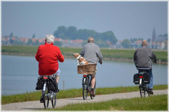 Three elderly people riding bikes on a path near a body of water.
