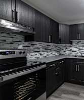 a black and white photo of a kitchen with black cabinets and stainless steel appliances