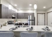 Thumbnail 2 of 8 - A modern kitchen with a white countertop and grey chairs.