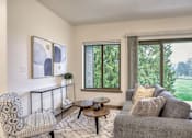 Thumbnail 5 of 8 - A living room with a grey couch, a black and white patterned chair, a small table with a vase on it, and a painting on the wall.