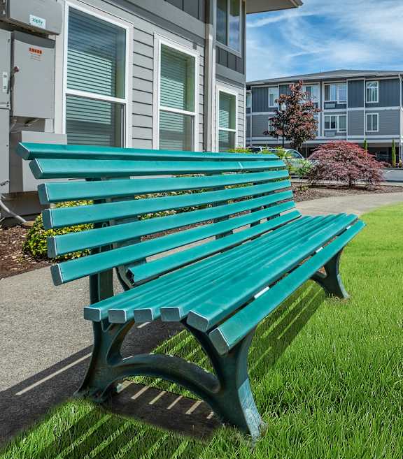 A green bench is in the foreground of a grassy area. at Fairview Village Apartments, Fairview, Oregon