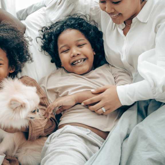 A family is lying on a bed with a small dog.