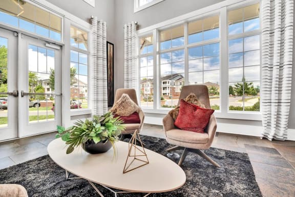 a living room with two chairs and a table and windows