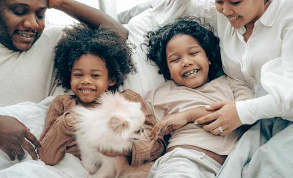 A family is lying on a bed with a small dog.