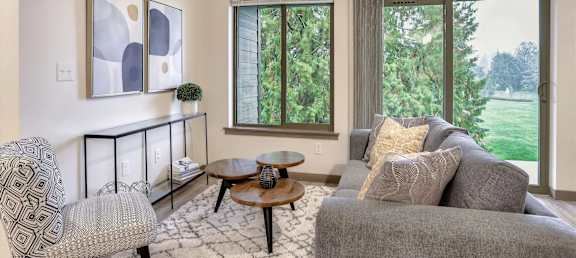 A living room with a grey couch, a black and white patterned chair, a small table with a vase on it, and a painting on the wall.