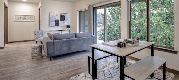 A living room with a grey couch, a white table, and a large window.