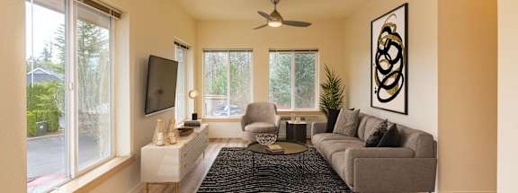 A living room with a grey couch, a black rug, and a ceiling fan. at Fairview Village Apartments, Fairview, OR, 97024