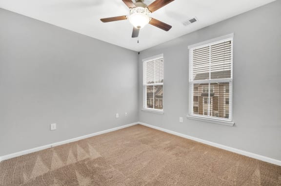 an empty living room with a ceiling fan and two windows