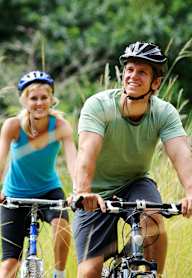 A man and a woman are riding bicycles in a field.