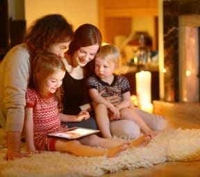 Family Sitting on Floor Together Playing on Tablet Next to Fireplace