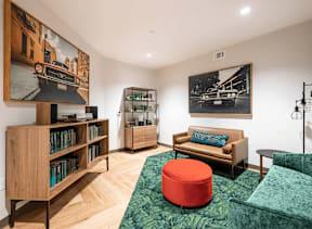 A living room with a green couch and a red ottoman.