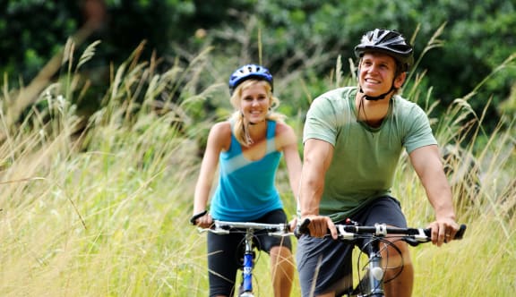 a man and a woman riding bikes through a grassy field