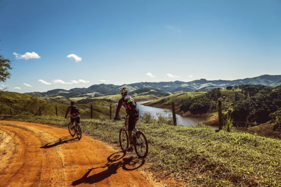 Men Riding Bikes on Path with Beautiful View of River and Mountains